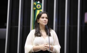 Deputada Maria Arraes fala ao microfone. Ela é clara, tem cabelos escuros, lisos e compridos; e usa uma blusa bege